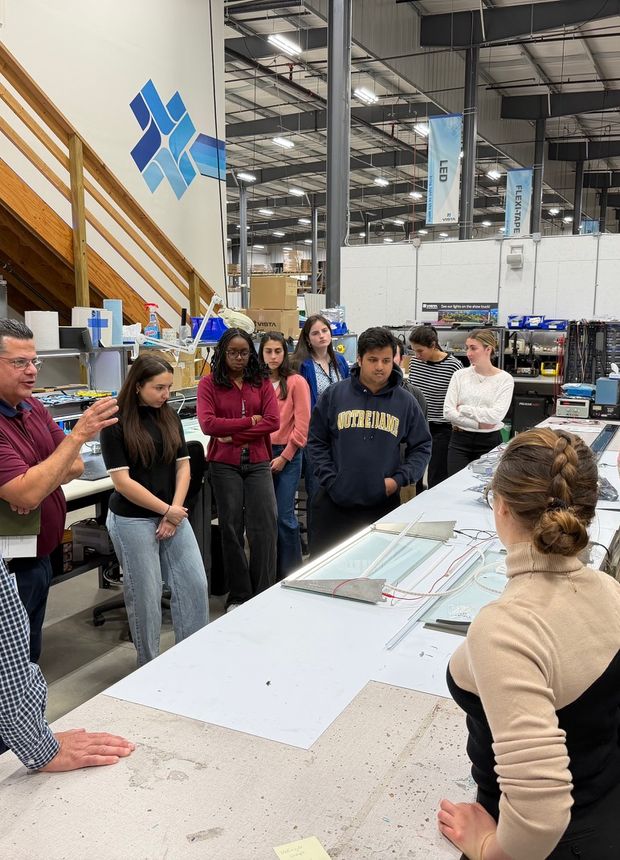 Fellows and plant staff gathered around a layout table during the Vista Manufacturing tour