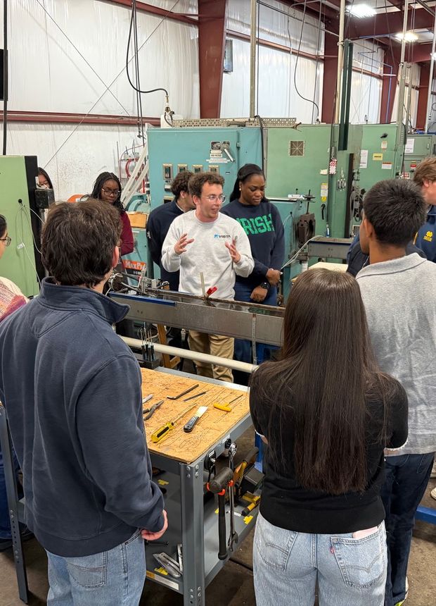 Fellows at a workbench with an engineer during the plant tour